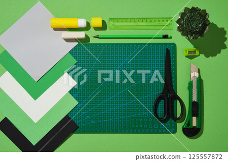 Top view of the paper crafts work table in green theme. Scissors, craft knife, pencil, eraser, cutting mat, colored paper. Space for text. Top view of the paper crafts work table in green theme. Scissors, craft knife, pencil, eraser, cutting mat, colored paper. Space for text. 125557872