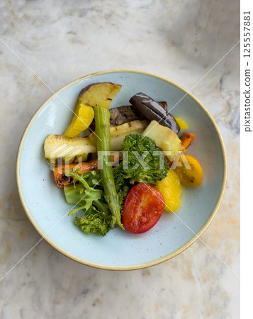 Colorful roasted vegetables including broccoli, tomato, zucchini, asparagus and carrots served in a light blue ceramic bowl perfect for healthy eating, vegan meals, food photography and culinary menus 125557881