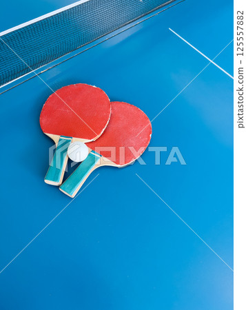 Table tennis paddles and ball resting on a clean blue court with visible net representing active sports, leisure recreation, competitive gaming and healthy indoor activities for all ages 125557882