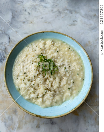 Delicious creamy lemon risotto served in a light blue ceramic bowl placed on a marble surface featuring fresh herbs garnish perfect for gourmet cuisine, restaurant menus or culinary content creation 125557892