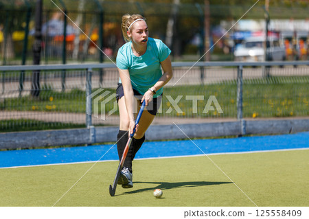 Young sportswoman leading the ball at the field hockey game 125558409