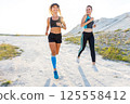 Two athletic woman enjoy outdoor running in sunlight against a scenic backdrop 125558412