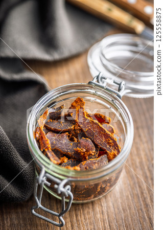 Beef jerky. Dried spiced meat in jar on wooden table. 125558875