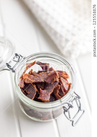 Beef jerky. Dried spiced meat in jar on white table. 125558876
