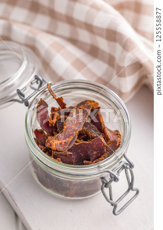 Beef jerky. Dried spiced meat in jar on white table. 125558877
