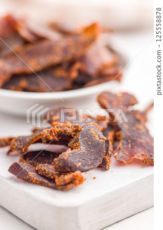 Beef jerky. Dried spiced meat on white table. 125558878