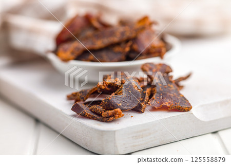 Beef jerky. Dried spiced meat on white table. Beef jerky. Dried spiced meat on white table. 125558879