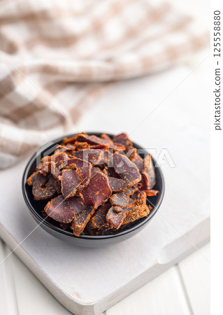 Beef jerky. Dried spiced meat in bowl on white table. 125558880