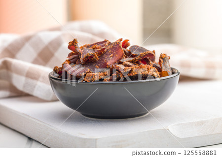 Beef jerky. Dried spiced meat in bowl on white table. Beef jerky. Dried spiced meat in bowl on white table. 125558881