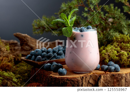 Blueberry smoothie in glass and fresh berries on a pine stump. Blueberry smoothie in glass and fresh berries on a pine stump. 125558967