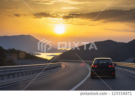 Road on Peljesac peninsula in Croatia, Europe. Scenic Road Trip: Driving into the sunset with mountains and water views on a winding coastal highway. Freedom and adventure awaits! 125558971