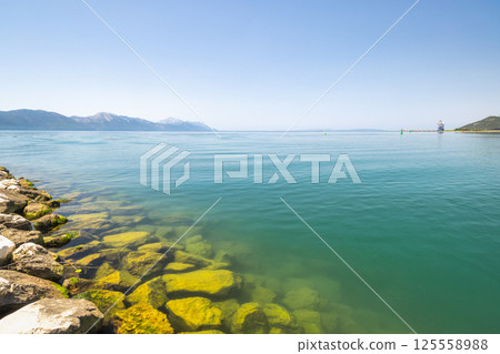 Neretva river near the mouth of river into Adriatic Sea, Croatia, Europe. Tranquil turquoise sea with rocky coastline, distant mountains under a clear blue sky, evoking serenity and beauty of nature. 125558988