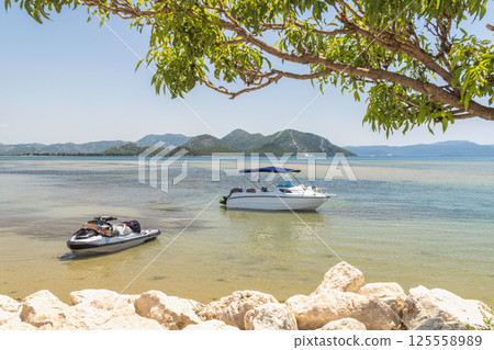Delta of the Neretva river near the mouth of river into Adriatic Sea, Croatia, Europe. Idyllic coastal scene with a boat and jet ski gently floating on clear waters. Delta of the Neretva river near the mouth of river into Adriatic Sea, Croatia, Europe. Idyllic coastal scene with a boat and jet ski gently floating on clear waters. 125558989