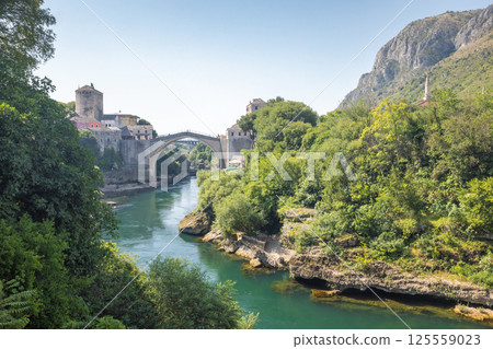 The Stari Most bridge, old bridge on Neretva river in Mostar town, Bosnia and Herzegovina, Europe. Scenic view of a stone bridge and river surrounded by lush greenery, old buildings, and mountains. The Stari Most bridge, old bridge on Neretva river in Mostar town, Bosnia and Herzegovina, Europe. Scenic view of a stone bridge and river surrounded by lush greenery, old buildings, and mountains. 125559023