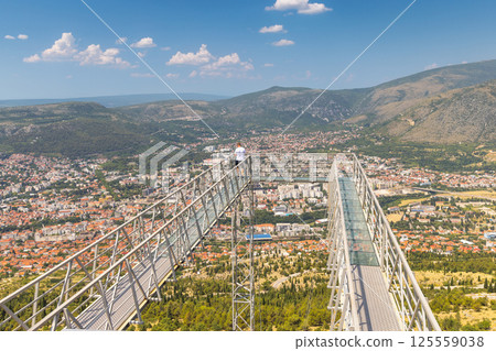 View of Mostar from the Fortica hill, Bosnia and Herzegovina, Europe. Stunning view of a city and mountains from a modern skywalk, featuring steel construction and a single figure enjoying panorama. 125559038