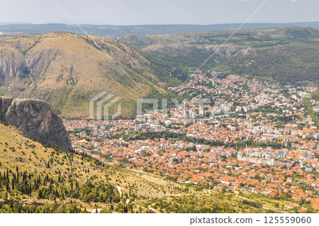 View of Mostar from the Fortica hill, Bosnia and Herzegovina, Europe. Scenic overlook of a city nestled in a valley, showing the urban architecture surrounded by hills and mountains. 125559060
