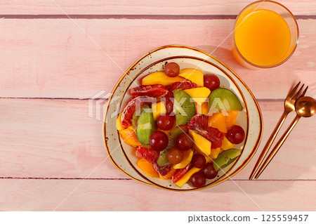 Fruit salad with kiwi, mango, grapes, nuts, citrus fruits with chia seeds for weight loss and a glass of orange juice. Healthy breakfast with ingredients, kitchen background. Natural nutrition and 125559457