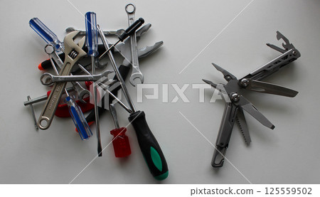 Multitool and a stack of variety hand tools on different sides of a white table 125559502