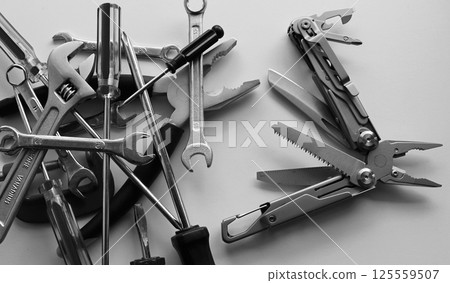 Black and white image of blades and screws of steel multi-tool VS pile of hand tools dumped in disarray Black and white image of blades and screws of steel multi-tool VS pile of hand tools dumped in disarray 125559507