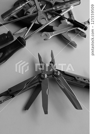 Folding utility multi-tool with opened blades against a bunch of unnecessary tools monochrome stock image Folding utility multi-tool with opened blades against a bunch of unnecessary tools monochrome stock image 125559509