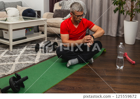 Man checking fitness tracker during home workout session Man checking fitness tracker during home workout session 125559672