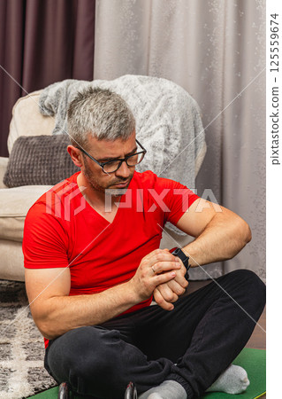 Man checking smartwatch while exercising at home Man checking smartwatch while exercising at home 125559674