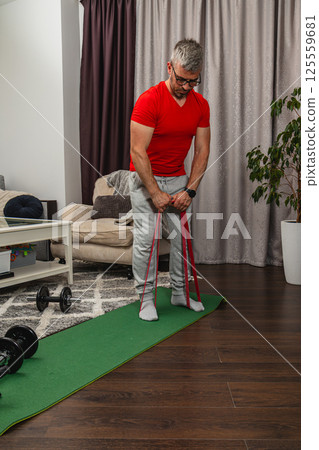 Man performs resistance band workout in living room Man performs resistance band workout in living room 125559681