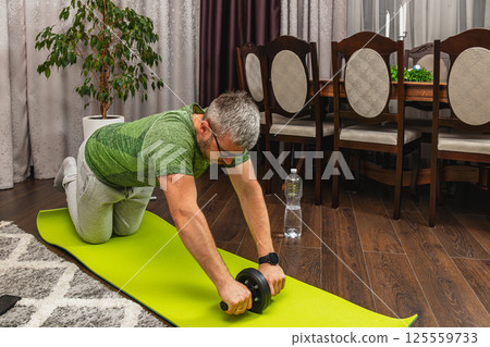 Man exercising indoors with an ab roller on yoga mat Man exercising indoors with an ab roller on yoga mat 125559733