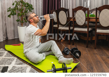 Man resting after workout and drinking water at home Man resting after workout and drinking water at home 125559740