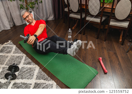 Man exercising at home with dumbbells and mat Man exercising at home with dumbbells and mat 125559752