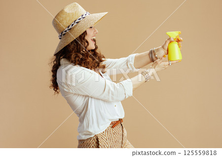 smiling female in blouse and shorts aiming as gun on beige 125559818