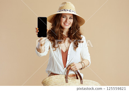 happy woman showing smartphone blank screen on beige 125559821