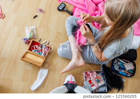 Cute teenager girl blonde hair sits floor sewing pink black fur costume piece. Child making homemade furry dragon mask. Quadrobic Therian fandom subculture. Design hobby creative artwork 125560205
