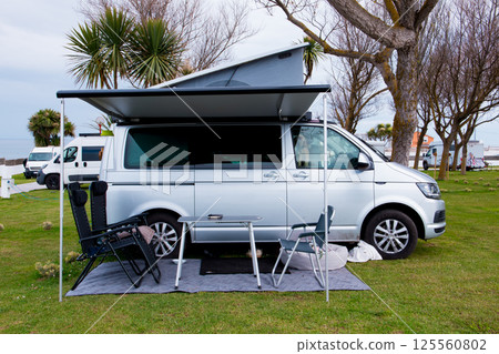 Camper van setup with awning and chairs in scenic campsite Camper van setup with awning and chairs in scenic campsite 125560802