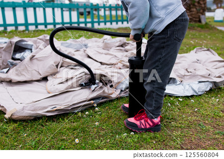 Child inflating tent with pump in outdoor park setting 125560804