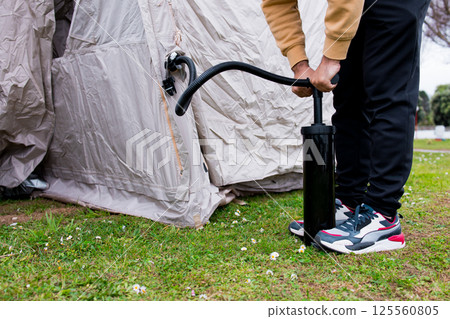 Young hispanic adult male inflating tent outdoors with hand pump 125560805