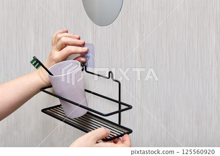 Person is positioning transparent adhesive hook on wall above metal bathroom shelf during marking process before final installation and attachment. Person is positioning transparent adhesive hook on wall above metal bathroom shelf during marking process before final installation and attachment. 125560920