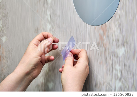 Person peels off transparent protective layer from nano adhesive hook, preparing surface of hook for application to plastic wall panel. 125560922