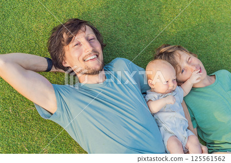 Father, older son, and newborn baby on a meadow in the park. Family spending quality time together in nature. Parenthood, love, and family bond concept 125561562