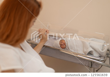 A young mother admires her newborn son in the maternity hospital.  125561639