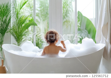 Toddler enjoys bubble bath in bright family bathroom with parental supervision and natural light 125561712