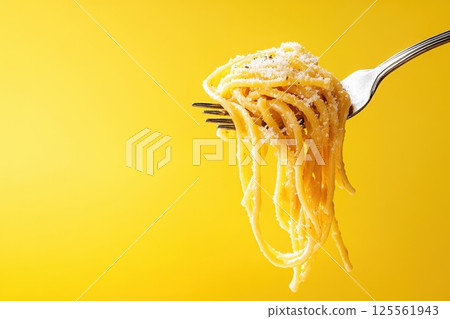 Pasta strands twirled with fork against bright yellow background 125561943