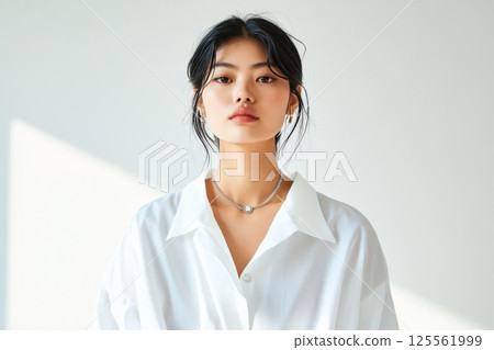 Model of East Asian descent showcases statement necklace in minimalist setting with natural light 125561999