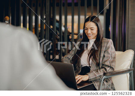 A Positive Businesswoman Is Smiling While Using Her Laptop in a Modern Office Setting A Positive Businesswoman Is Smiling While Using Her Laptop in a Modern Office Setting 125562328