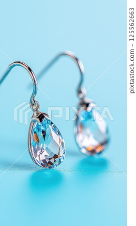 Platinum drop earrings with teardrop sapphires shining against a soft blue background 125562663