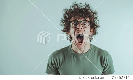 Portrait of a furious young man with curly hair and eyeglasses shouting and showing negative emotions against a light blue background, expressing anger and frustration Portrait of a furious young man with curly hair and eyeglasses shouting and showing negative emotions against a light blue background, expressing anger and frustration 125562715