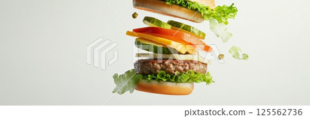 Tasty burger exploding with fresh ingredients such as lettuce, tomato, pickles, cheese, and a juicy beef patty, creating a visually appealing fast food concept against a white background 125562736
