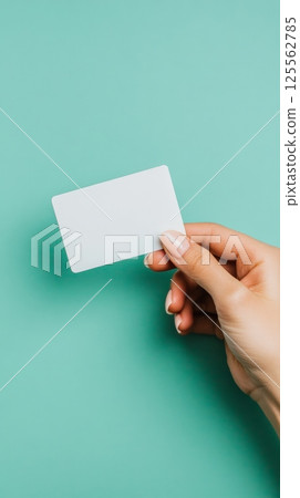 Hand of a manager holding a levitating blank business card on a turquoise background, ideal for showcasing contact information or promotional messages 125562785