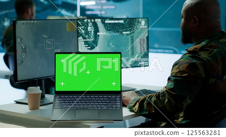 IT expert collecting real time information next to isolated chroma key screen, high tech gear in command post. Soldier processing intelligence for field operations and strategic missions. Camera A. IT expert collecting real time information next to isolated chroma key screen, high tech gear in command post. Soldier processing intelligence for field operations and strategic missions. Camera A. 125563281