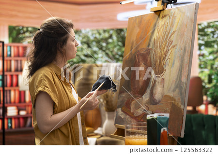 Woman with talent painting a rustic masterpiece and using fabric to clean her brush after changing the color. Artist feeling inspired to try a new painting technique in art and craft workshop. 125563322